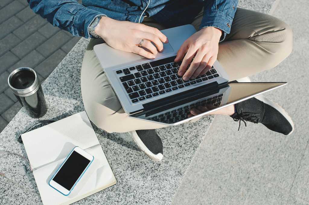 remote millennial working on laptop with coffee outside